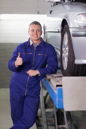 Man standing next to a car with his thumb up in a garageの写真素材