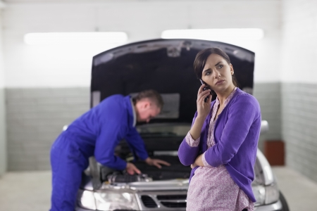Client holding a mobile phone next to a car in a garageの写真素材