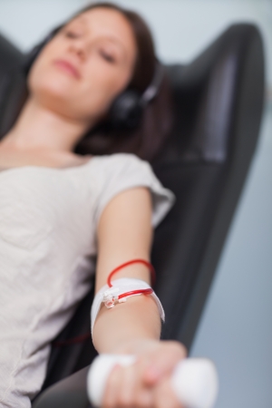 Patient listening to music while giving her blood in a hospital roomの写真素材