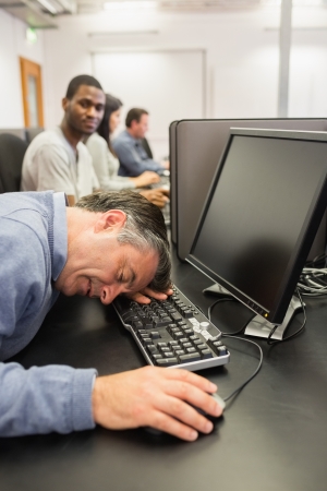 Man taking nap at computer class on the keyboard in collegeの写真素材