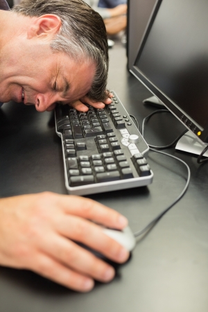 Man asleep on keyboard hand on mouse in computer classの写真素材