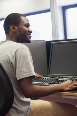 Student sitting at computer desk and smiling in computer room in collegeの写真素材
