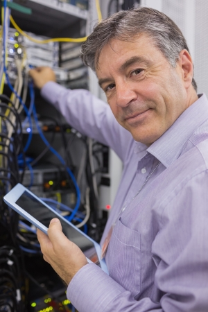 Man smiling while doing server maintenance with tablet in hallwayの写真素材