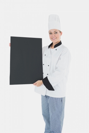 Portrait of happy female chef holding black billboard over white backgroundの写真素材