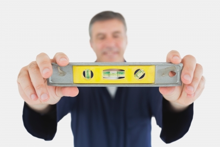Mature male technician holding spirit level over white background