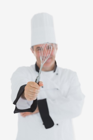 Mature chef showing wire whisk over white backgroundの写真素材