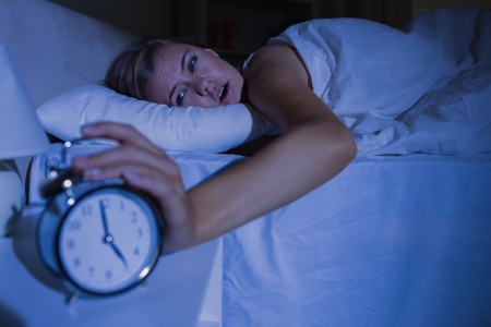 Awakening woman stopping her alarm clock at night in the bedroomの写真素材
