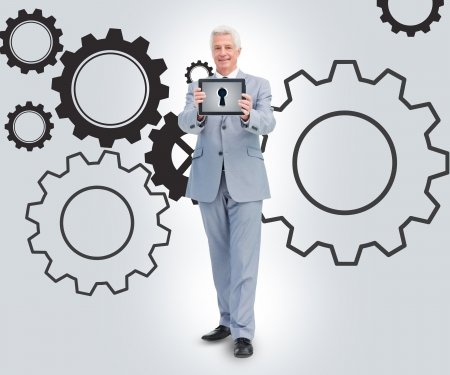 Businessman holding tablet standing against a cogs backgroundの写真素材