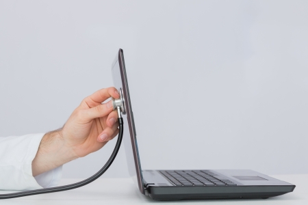 Close-up of hand examining laptop with stethoscope against plain background