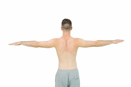 Rear view of young shirtless man standing with arms outstretched over white backgroundの写真素材