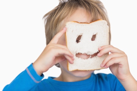 Young boy looking through holes in bread slice over white background