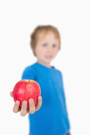 Young boy holding out a apple over white backgroundの写真素材