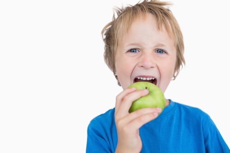 Portrait of young boy eating green apple over white backgroundの写真素材