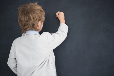 Rear view of young boy dressed as teacher writes on black boardの写真素材