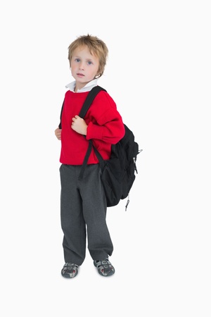 Portrait of young boy with schoolbag standing against white backgroundの写真素材