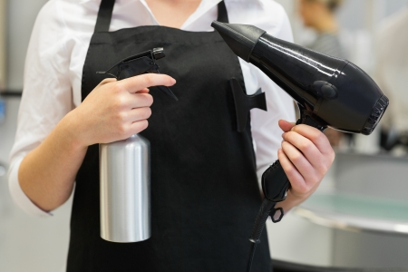 Close-up of female hairdresser holding hair dryer and sprayの写真素材