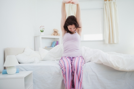 Sleepy young woman waking up in bed and stretching her arms upの写真素材