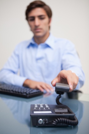 Young business man with telephone receiver at office deskの写真素材