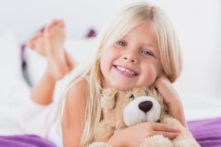 Little girl with her teddy bear lying on a bed in the bedroomの写真素材