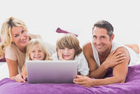 Smiling family using laptop on a bedの写真素材