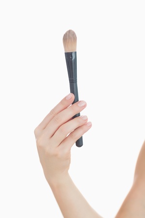 Close-up of hand holding make-up brush over white backgroundの写真素材