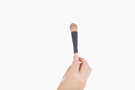 Close-up of hand holding make-up brush over white backgroundの写真素材
