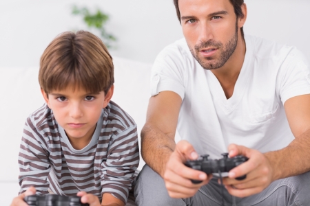 Focused father and son playing video games together on the couchの写真素材