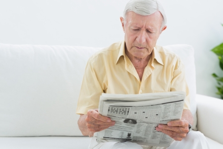 Elderly concentrated man reading newspapers on a sofaの写真素材