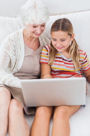 Smiling girl using laptop with granny on the couchの写真素材
