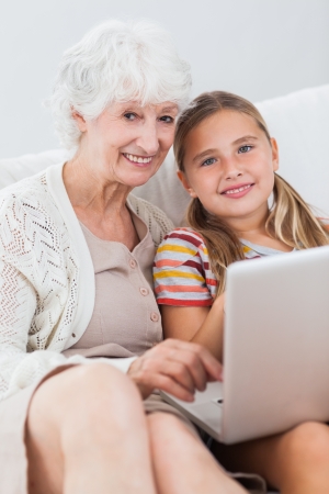 Happy girl using laptop with granny on the couchの写真素材