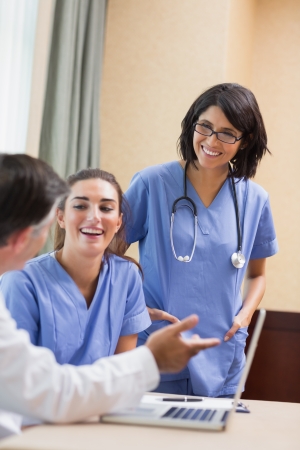 Nurses laughing with doctor using laptop in a meetingの写真素材
