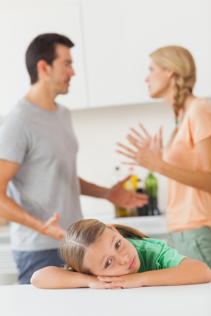 Couple arguing behind a sad girl in the kitchenの写真素材