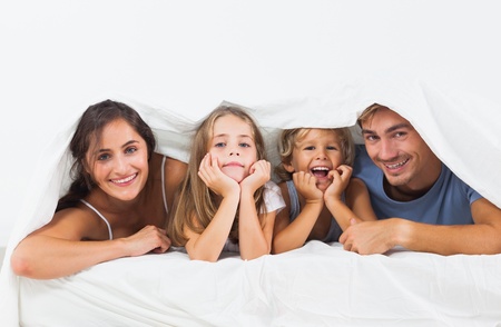 Family in the duvet smiling on the bedの写真素材