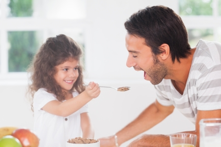 Little girl feeding cereal to father in kitchenの写真素材
