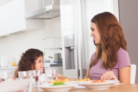Smiling girl and her mother at the dinner table in kitchenの写真素材