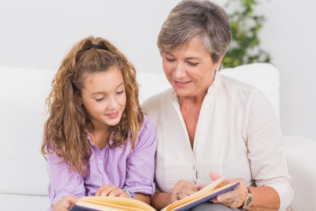 Portrait of a child and her grandmother reading a book in sitting roomの写真素材