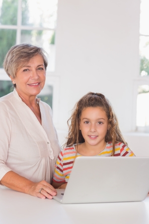 Smiling grandmother and child looking at camera together with laptop in kitchenの写真素材