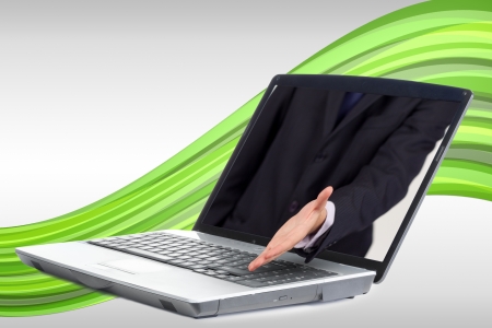 Businessman reaching out from laptop for handshake on green wave backgroundの写真素材