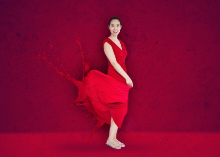 Happy asian woman with red dress turning to paint splatter on deep red backgroundの写真素材