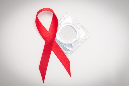 Red Aids ribbon beside condom on white backgroundの写真素材