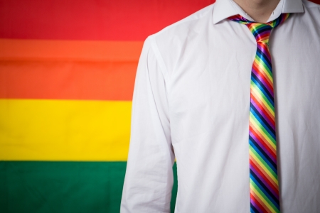 Man wearing shirt and rainbow tie on rainbow flag backgroundの写真素材