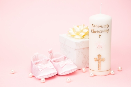 Christening candle with pink baby booties and gift box on pink background with pearlsの写真素材