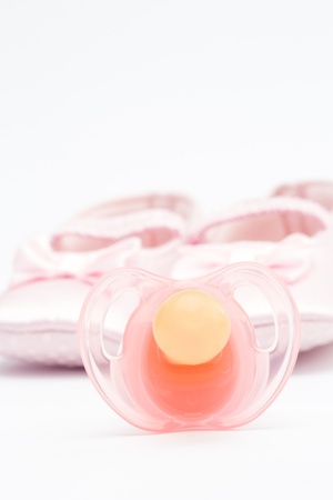 Pink soother with baby booties on white background