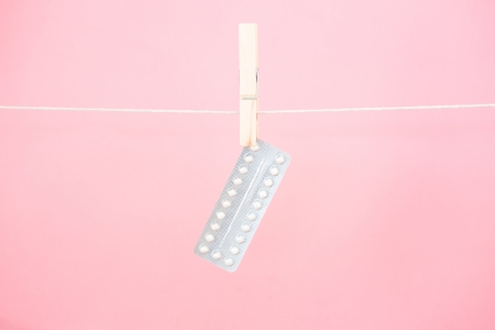 Contraceptive pill blister pack hanging from line on pink backgroundの写真素材