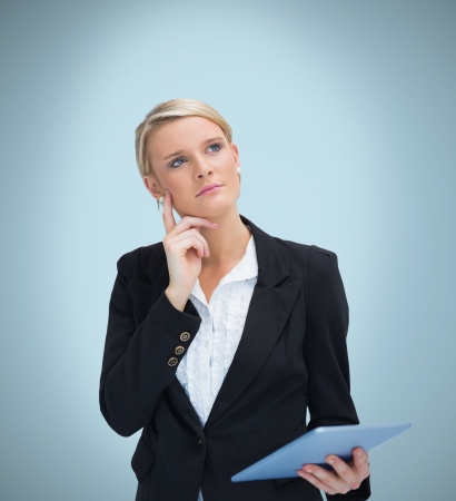 Thoughtful businesswoman with tablet pc on blue backgroundの写真素材