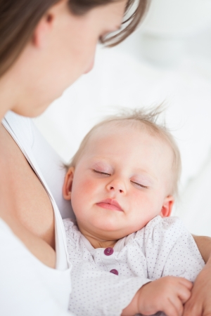 Cute baby sleeping in the arms of her mother in a bedroomの写真素材