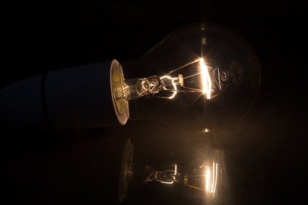 Light bulb without glass turned over on black background on reflective surfaceの写真素材