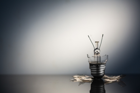Shattered light bulb standing with copy space on reflective surface