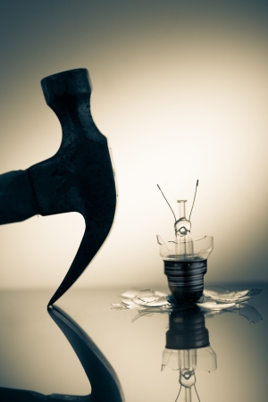 Hammer silhouette beside broken light bulb on reflective surfaceの写真素材