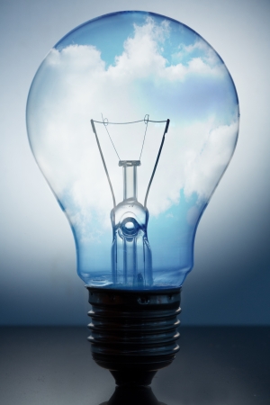 Close up of big light bulb standing with bright blue sky with clouds in itの写真素材